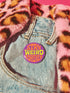 A round metal pin button with a glossy finish and a vibrant purple background. The phrase 'STAY WEIRD FOREVER' is written across the center in a wavy, psychedelic 70s-style font. The words 'STAY' and 'FOREVER' are a bold, bright orange, while the word 'WEIRD' is rendered in a contrasting, electric chartreuse lime green. The button has a smooth, scratch-resistant mylar surface covering the design. The pin is shown in its 2-inch and 3-inch variations, highlighting its circular shape and durable construction.